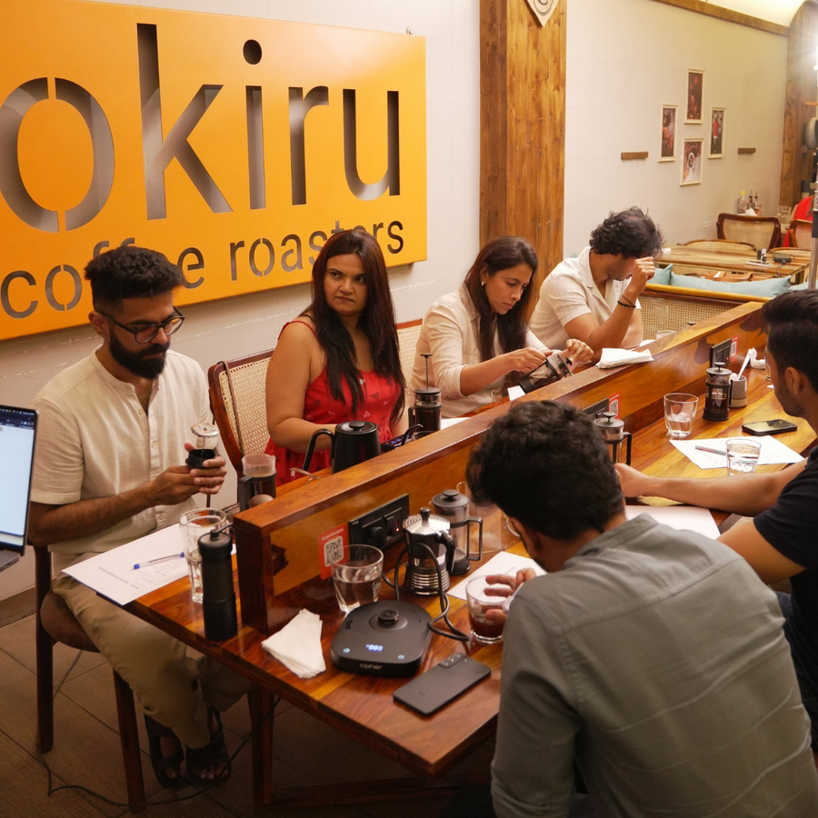 People sitting at a counter in a coffee shop with 'okiru' branding on the wall attending coffee brewing workshop