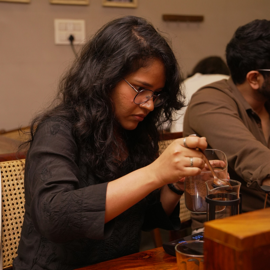 Woman sitting at a table with a glass jar of coffee and a french press, engaged in an activity.