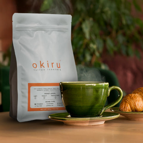 okiru coffee bag with a green cup and croissant on a wooden table
