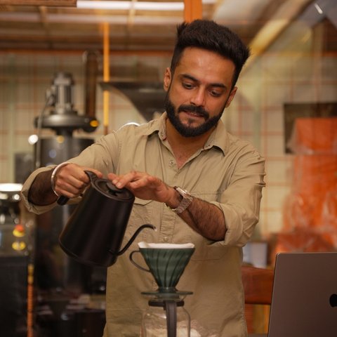 Man preparing coffee in a kitchen setting with a kettle and pourover