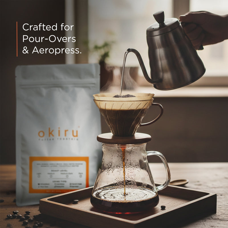 Coffee being poured from a kettle into a glass carafe with 'okiru' coffee package in the background.