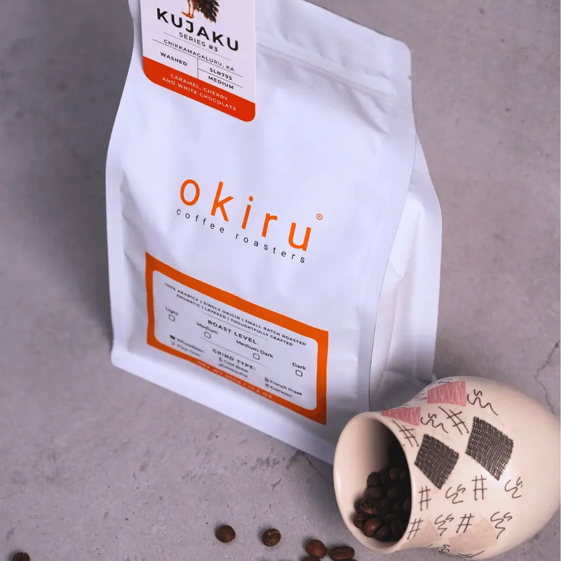okiru coffee roasters bag with a ceramic cup filled with coffee beans on a gray surface